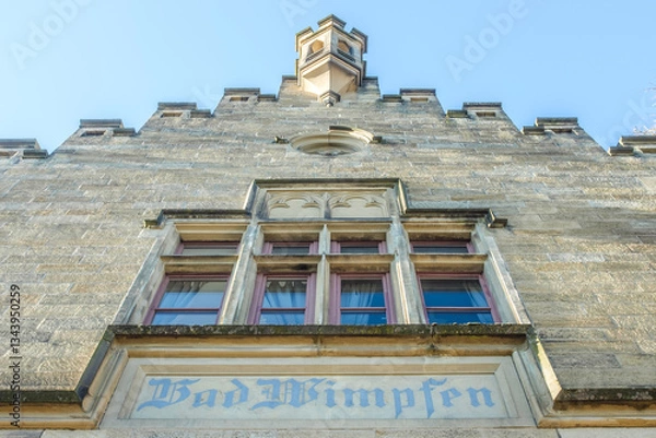 Obraz Neugotische Sandstein-Hausfassade mit Staffelgiebel und Erker des Empfangsgebäudes des Bahnhofes in Bad Wimpfen am Berg vor blauem Himmel in Untersicht