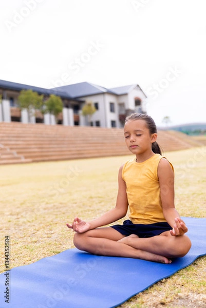 Obraz Girl meditating on yoga mat outside school, practicing mindfulness and relaxation, copy space