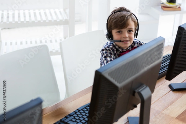 Obraz Young boy using computer and headset in office, engaging in online learning, copy space