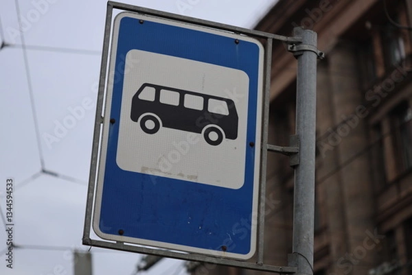 Fototapeta Street sign featuring a blue and white design with a bus passing by.