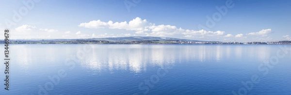 Fototapeta Clear day.  Lake Zug in central Switzerland. Clouds are reflected in water lake. At the edge water is clear and see the bottom of the lake.