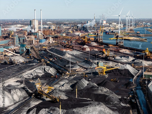 Obraz Steel industry in IJmuiden, Netherlands, showing coal storage, conveyors, and emissions. Wind turbines stand in contrast to fossil fuel-based production and industrial pollution. Aerial view.