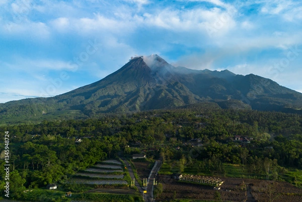 Fototapeta Drone photo showing the beauty of Mount Merapi in Sleman, Yogyakarta, Indonesia at sunrise. Aerial view of a volcano in the morning with a view of the forest and a branching road in front. 