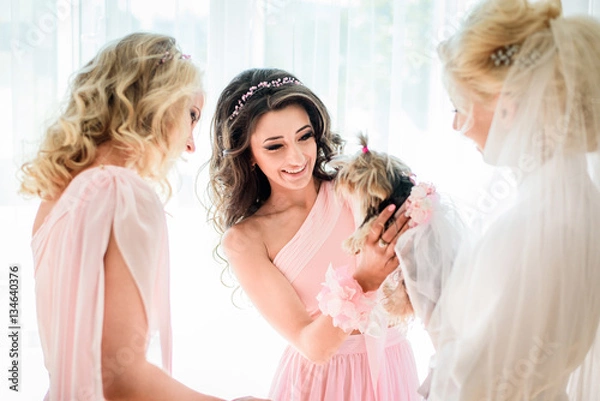 Obraz Bride and bridesmaids in pink dresses play with little fluffy do