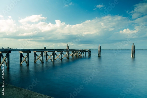 Fototapeta Clouds over a serene lake with a rustic wooden pier and smooth silky still blurred water