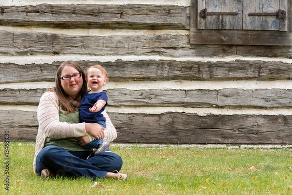 Obraz Happy mother and daughter sitting in the grass in front of an old house