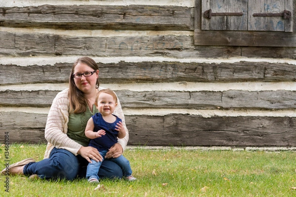 Obraz Happy mother and daughter sitting in the grass in front of an old house