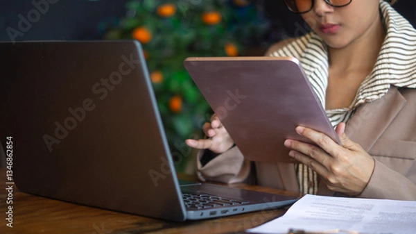 Obraz Businesswoman working diligently with technology devices in the office with tablet and laptop on the desk.