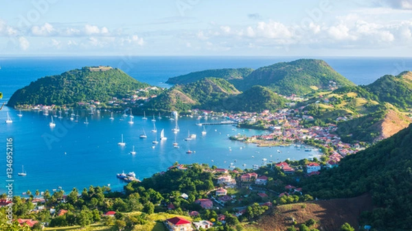 Fototapeta Vue de haut de la baie des Saintes en Guadeloupe avec la mer des Caraïbes, l'île de Terre de Haut, et des bateaux par une journée ensoleillée avec des nuages.
