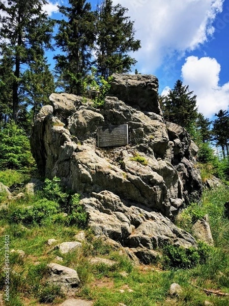 Fototapeta Rock formation with a historical plaque in Góry Sowie, Poland, surrounded by lush greenery and tall pines under a bright sky
