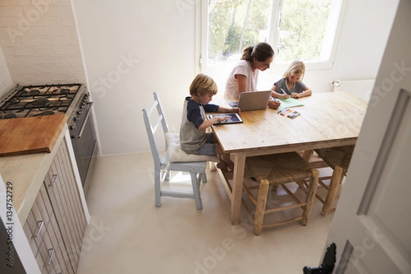 Fototapeta Mum and two kids working at kitchen table, elevated view