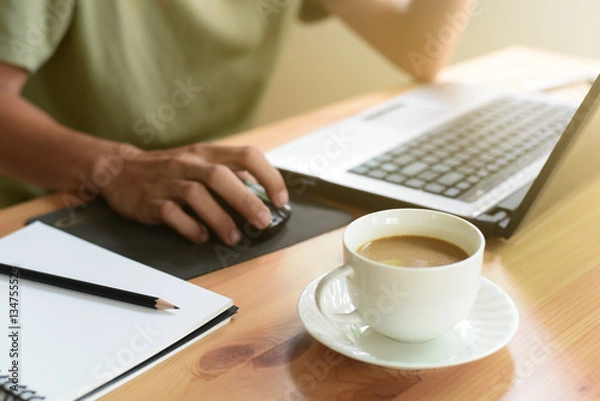 Obraz Close up of white coffee cup and hands of man working with computer