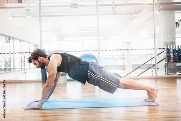 Fototapeta Side view of muscular man doing push up on mat
