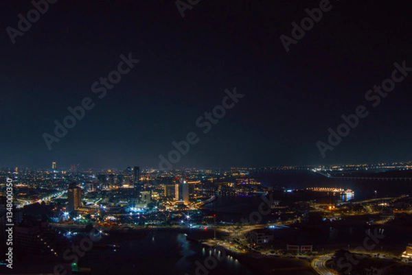 Fototapeta Aerial view of Abu Dhabi at night, showcasing the city's illuminated skyline, modern skyscrapers, and roads glowing under the night sky.