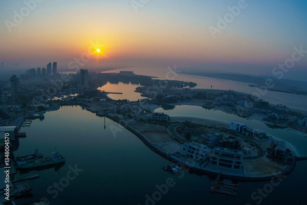 Fototapeta Aerial view of Abu Dhabi in the morning light, as the rising sun casts a golden glow over the city's modern skyline.