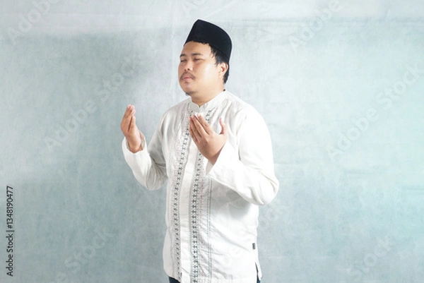 Fototapeta an Indonesian man is praying with his hands raised and wearing Muslim clothing