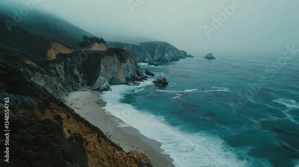 Fototapeta Coastal cliffs meet a beach under a foggy atmospheric sky