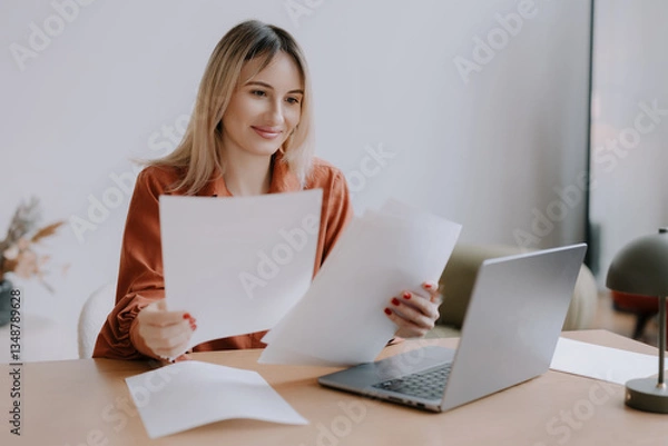 Fototapeta Woman reviewing documents at a desk with a laptop in a calm workspace during daytime