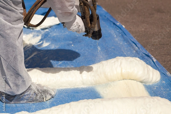 Fototapeta Technician spraying foam insulation using Plural Component Spray Gun