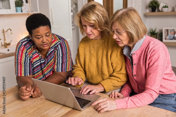 Obraz Senior Women Friends Gathering at Home. Three cheerful retired women enjoying friendly together in living room and chatting. Mature women use laptop computer typing on keyboard and pointing at screen