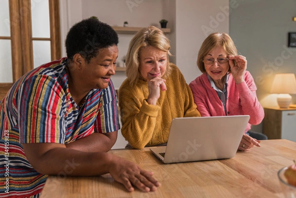 Obraz Senior Women Friends Gathering at Home. Three cheerful retired women enjoying friendly together in living room and chatting. Mature women use laptop computer typing on keyboard and pointing at screen