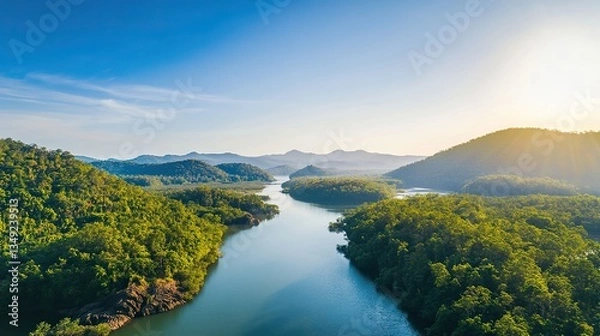 Fototapeta Aerial view of a wide river flanked by mangrove forests, with low flat mountains, green vegetation, rocks, clear sky and water reflecting in a charming, tranquil natural landscape.