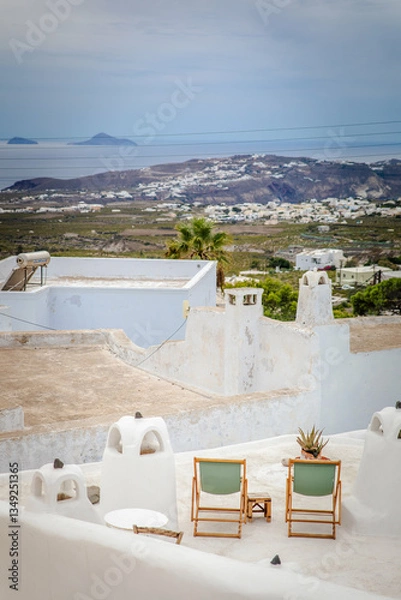 Fototapeta Vertical view of apartment terrace with sage green chairs and aloe plants in Pyrgos Kallistis, the island of Santorini, Greece, with panoramic vista of the Aegean Sea and islands and Greek isle coast