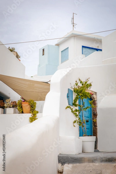 Fototapeta Vertical view of beautiful holiday apartment with turquoise blue door and terrace with plants in Pyrgos Kallistis in Santorini isle, Greece, a picturesque Greek village in mainland perfect for couples