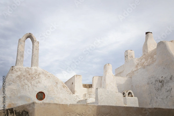 Fototapeta Horizontal photo of white-washed Greek traditional beautiful old house with tower, chimney and cloudy sky in Pyrgos Kallistis, Santorini, Greece - a hidden gem to explore in the Greek islands mainland