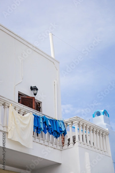 Fototapeta White washed traditional house in Pyrgos Kallistis in Santorini island, Greece, with blue laundry towels in greek colours drying on the clothesline outside of a window on a balcony with cloudy sky