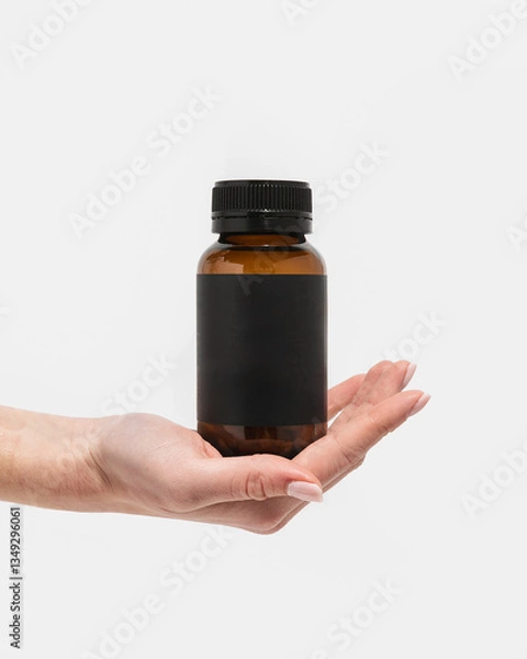 Obraz Woman's hand holding amber supplement bottle on white background