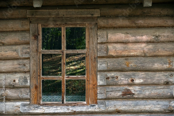 Fototapeta Rectangular window on the wall of a log house, the glass reflects the trees in the forest opposite. From the series Windows of the World.
