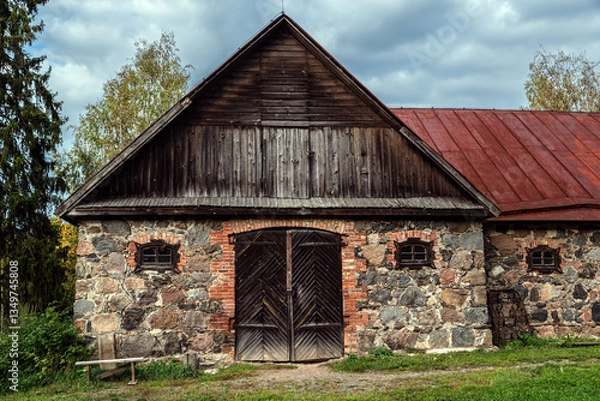 Fototapeta Old barn built of stones and bricks, with large wooden gates and small windows.
