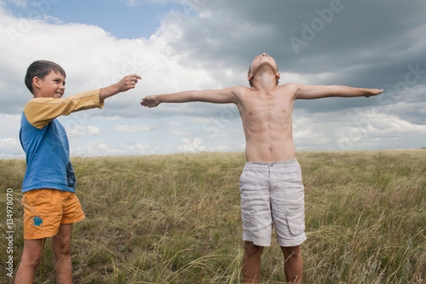 Fototapeta young boys playing in a field. boys in shorts. Boys stand in the desert. feather in the field. boy looking up at the sky. dreamer. two brothers. two friends. children playing in the field.
