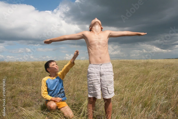 Fototapeta young boys playing in a field. boys in shorts. Boys stand in the desert. feather in the field. boy looking up at the sky. dreamer. two brothers. two friends. children playing in the field.
