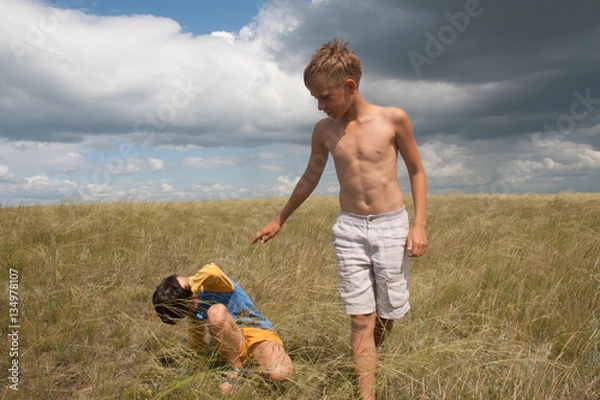 Fototapeta young boys playing in a field. boys in shorts. Boys stand in the desert. feather in the field. boy looking up at the sky. dreamer. two brothers. two friends. children playing in the field.
