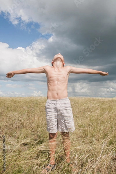 Fototapeta young boy stands in a field. boy in shorts. boy stands in the desert. feather in the field. boy looking up at the sky. dreamer