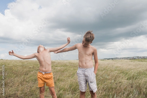 Fototapeta young boys playing in a field.  boys in shorts. Boys stand in the desert. feather in the field. boy looking up at the sky. dreamer. two brothers. two friends. children playing in the field.