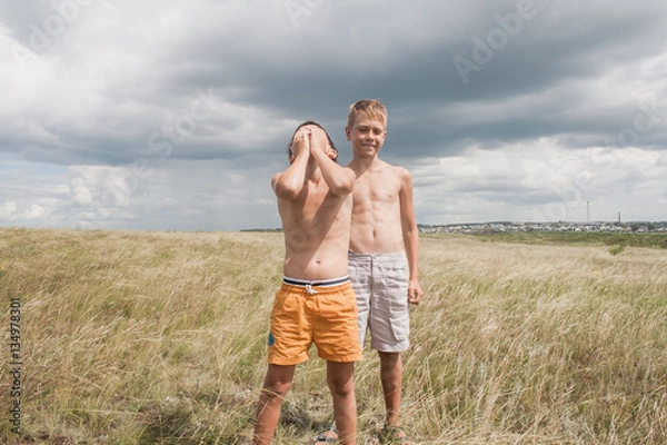 Fototapeta young boys standing in a field. boys in shorts. Boys stand in the desert. feather in the field. boy looking up at the sky. dreamer. two brothers. two friends. children playing in the field.