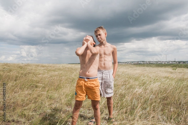 Fototapeta young boys standing in a field. boys in shorts. Boys stand in the desert. feather in the field. boy looking up at the sky. dreamer. two brothers. two friends. children playing in the field.