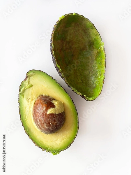 Fototapeta Ripe green avocado cut in half on white background, close-up, top view. One half is whole with a round brown pit, the other is empty, only the peel. Healthy eating.