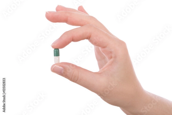 Fototapeta Hand holding a capsule or pill isolated on white.