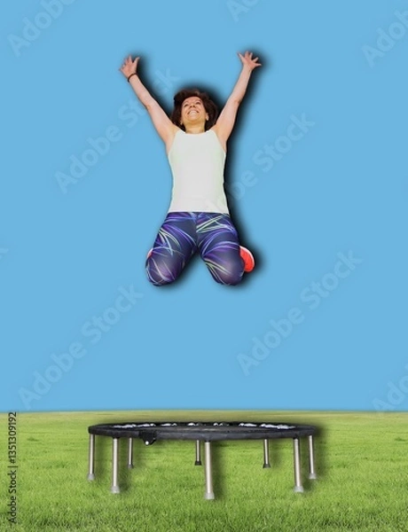 Fototapeta Woman Joyfully Jumping Above a Mini Trampoline in Outdoor Setting with a Blue Sky Background