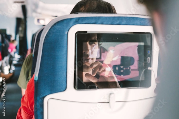 Fototapeta Reflection of a passenger on an airplane touch screen monitor while watching cartoon during long flight. Entertainment service system in aircraft