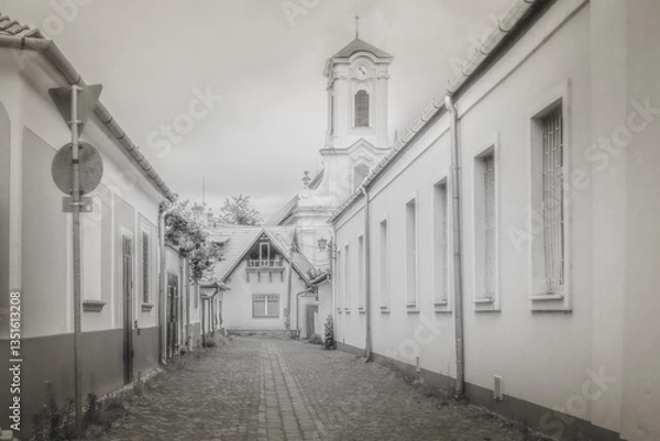Fototapeta A timeless street view of Szentendre, Hungary, featuring cobblestone paths and classic architecture. The baroque church tower in the background enhances the historic, nostalgic atmosphere