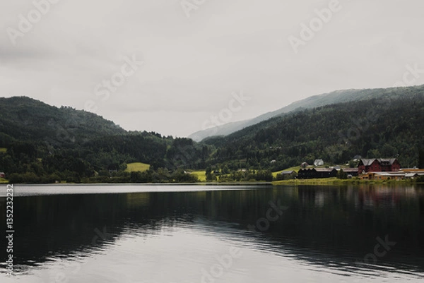 Obraz Norwegian fjord mountain landscape with a lake in the foreground and wooden houses on the shore. Overcast autumn day.