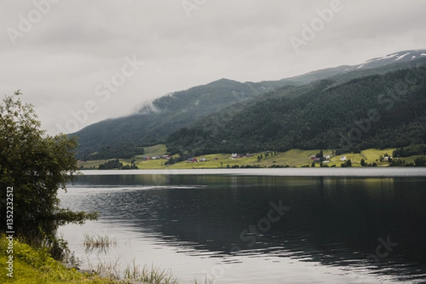 Fototapeta Norwegian fjord mountain landscape with a lake in the foreground and wooden houses on the shore. Overcast autumn day.