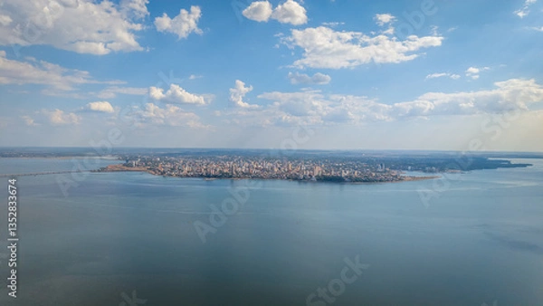 Fototapeta High angle aerial view of a densely populated area of Encarnación city, Paraguay, with the Paraná River and a distant view of Posadas city, Argentina, visible in the background.