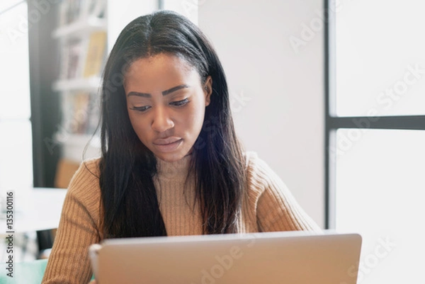 Fototapeta A beauty blogger is using modern smartphone and a portable computer for the work while sitting in a cafe. International student girl is studying online by a laptop connected to a wifi network.