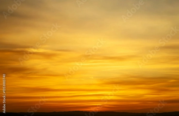 Fototapeta Golden hour sky with soft clouds and a dark horizon line in a warm and vibrant color palette